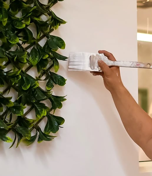 Painter cutting in a white interior wall beside greenery