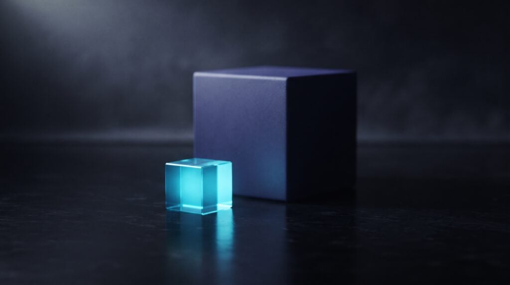 A small cyan-lit glass cube standing in front of a much larger unlit indigo cube of the same shape on a dark reflective surface