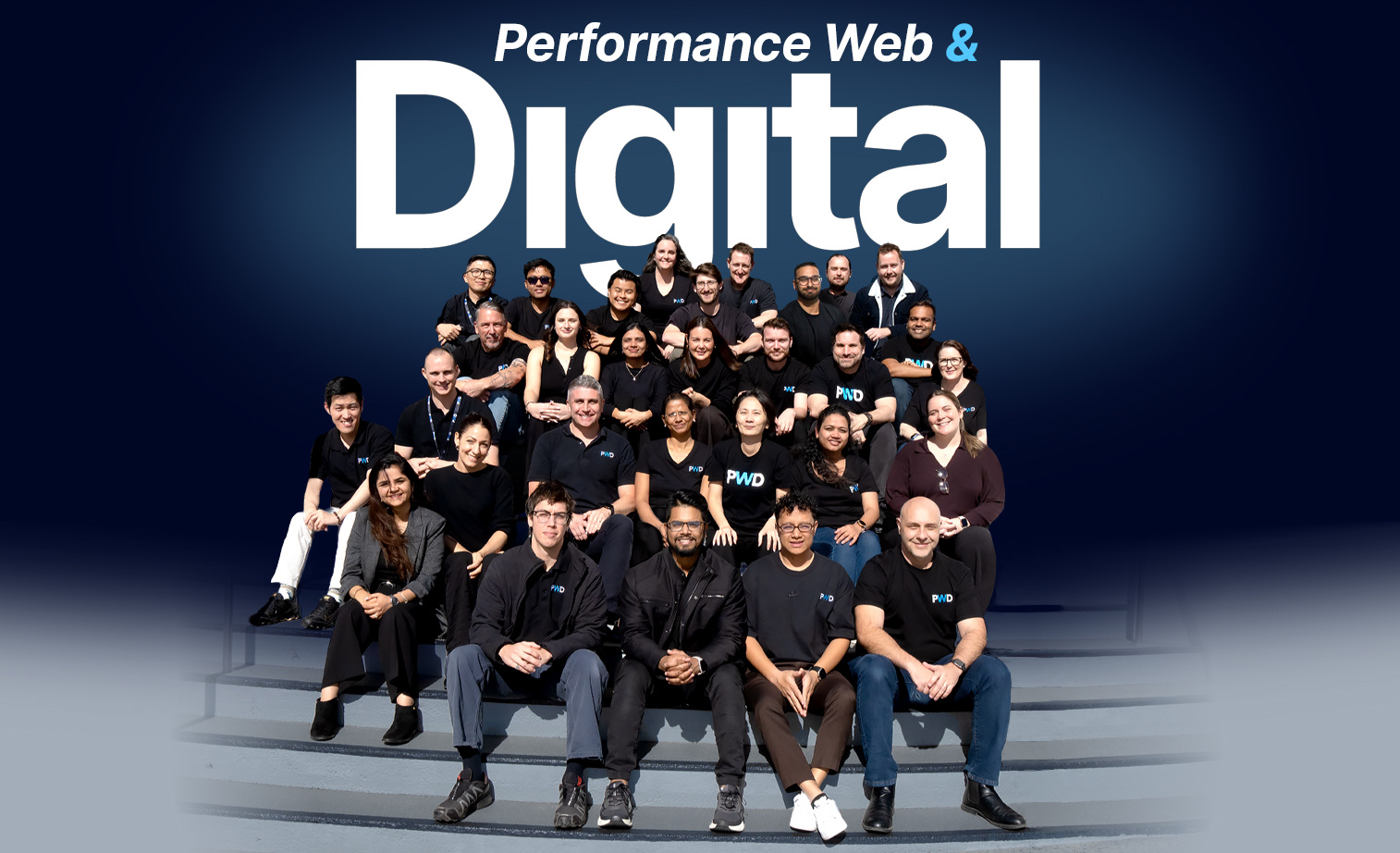 The PWD team in black PWD shirts sitting together on steps beneath the words Performance Web & Digital